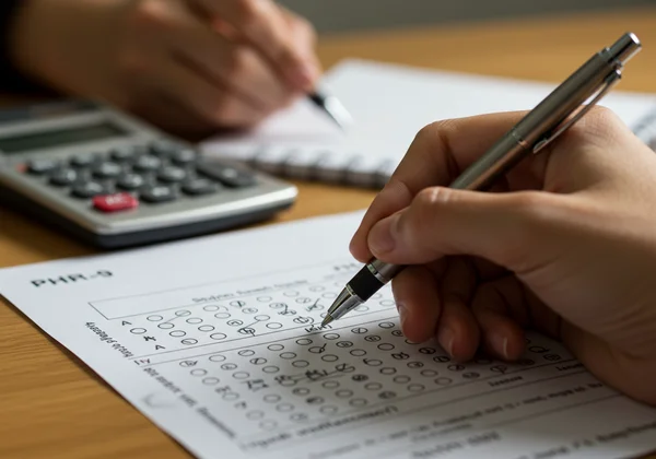 Manually scoring a PHQ-9 form with a pen and calculator.